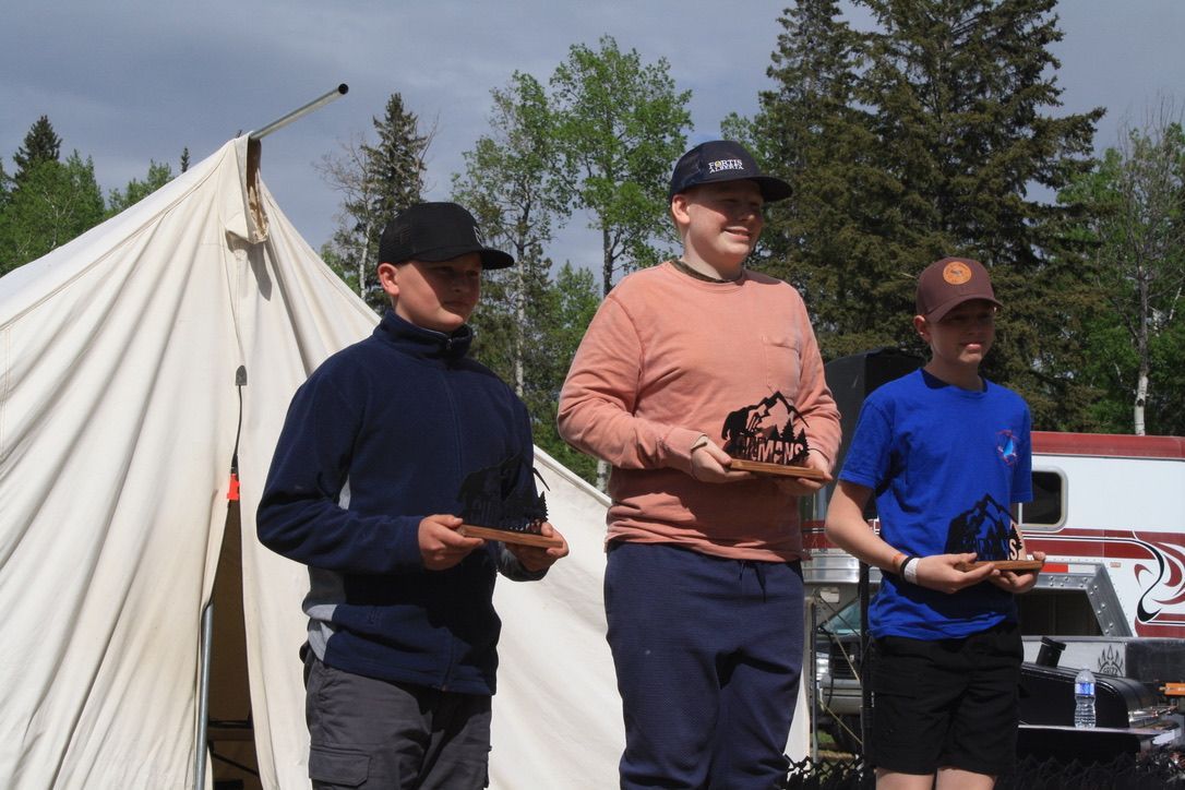 Three men standing in front of a tent holding trophies