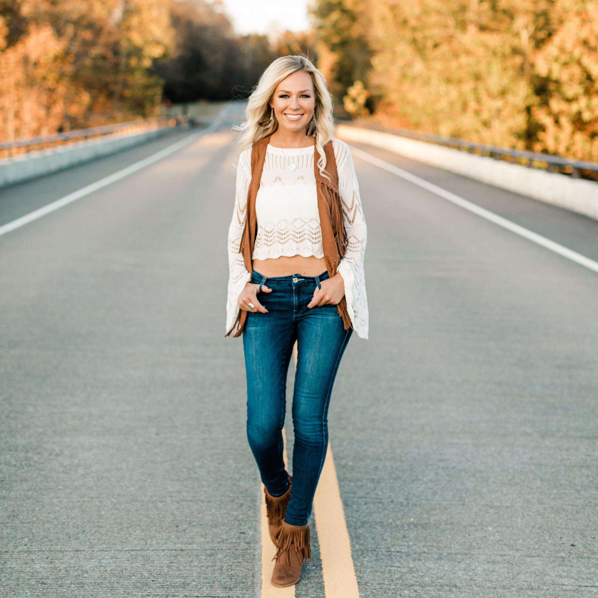 A woman is walking down a road wearing a crop top and jeans.