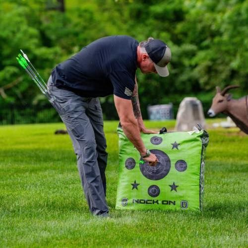 A man is standing next to a green target in a field.