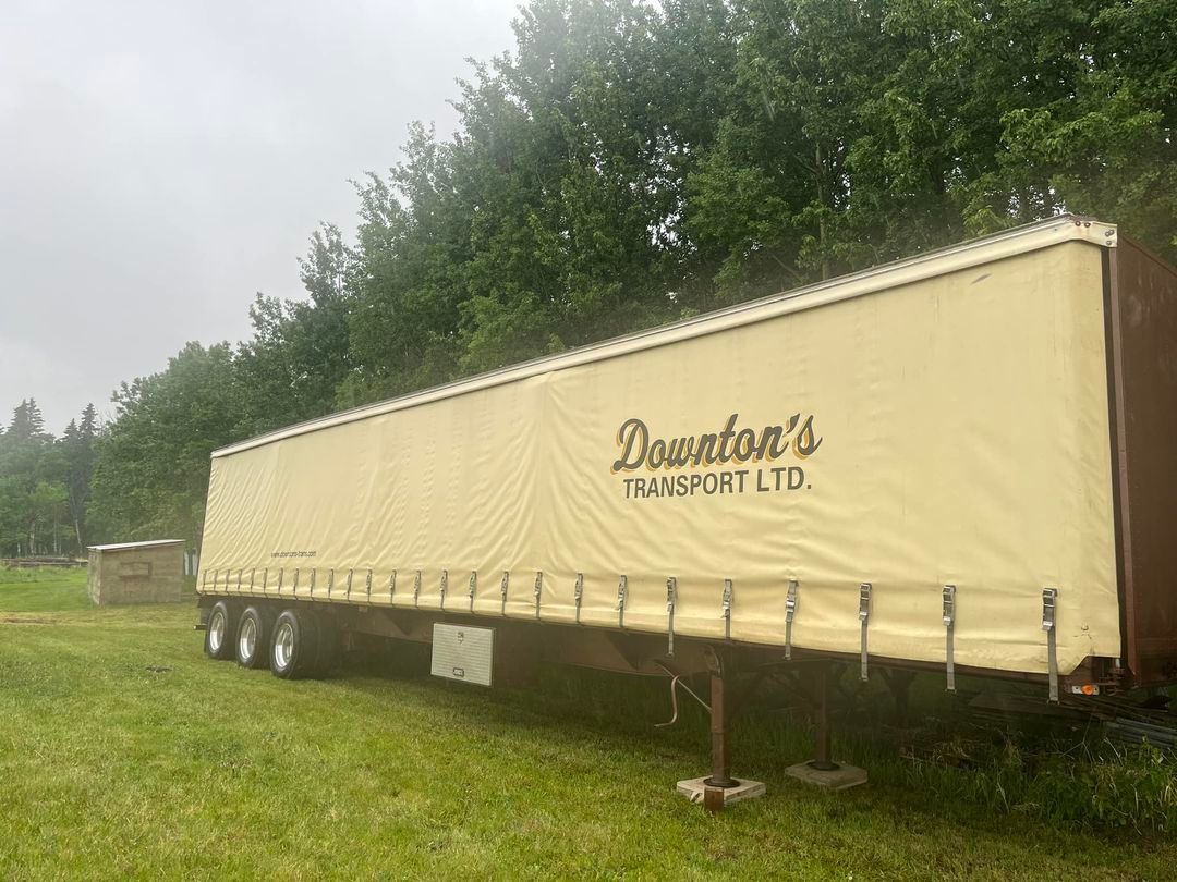 A trailer is parked in a grassy field with trees in the background.