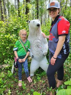 A woman and a little girl are standing next to a polar bear statue in the woods.