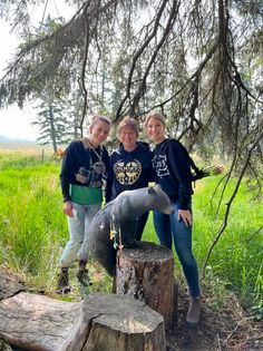 Three women are standing next to a statue of a raccoon on a tree stump.