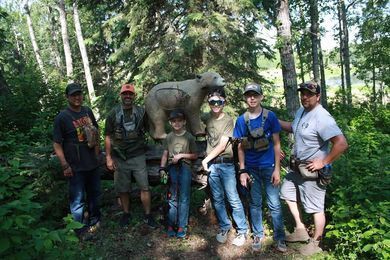 A group of people are standing in front of a bear statue in the woods.