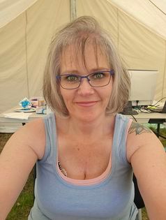 A woman wearing glasses is taking a selfie in front of a tent.