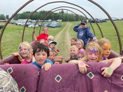 A group of children are riding in a wagon with their faces painted.