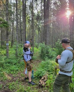 A man is taking a picture of another man in the woods.