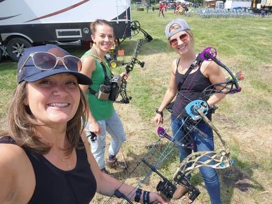Three women are standing in a field holding bows and arrows.