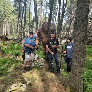 A group of people standing next to a statue of a bigfoot in the woods.