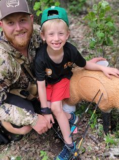 A man and a boy are kneeling next to a deer in the woods.