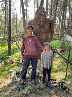 A man and a girl are standing next to a statue of a bigfoot in the woods.
