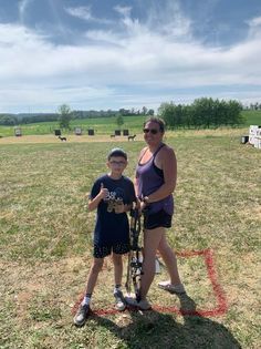 A woman and a boy are standing in a field holding bows and arrows.
