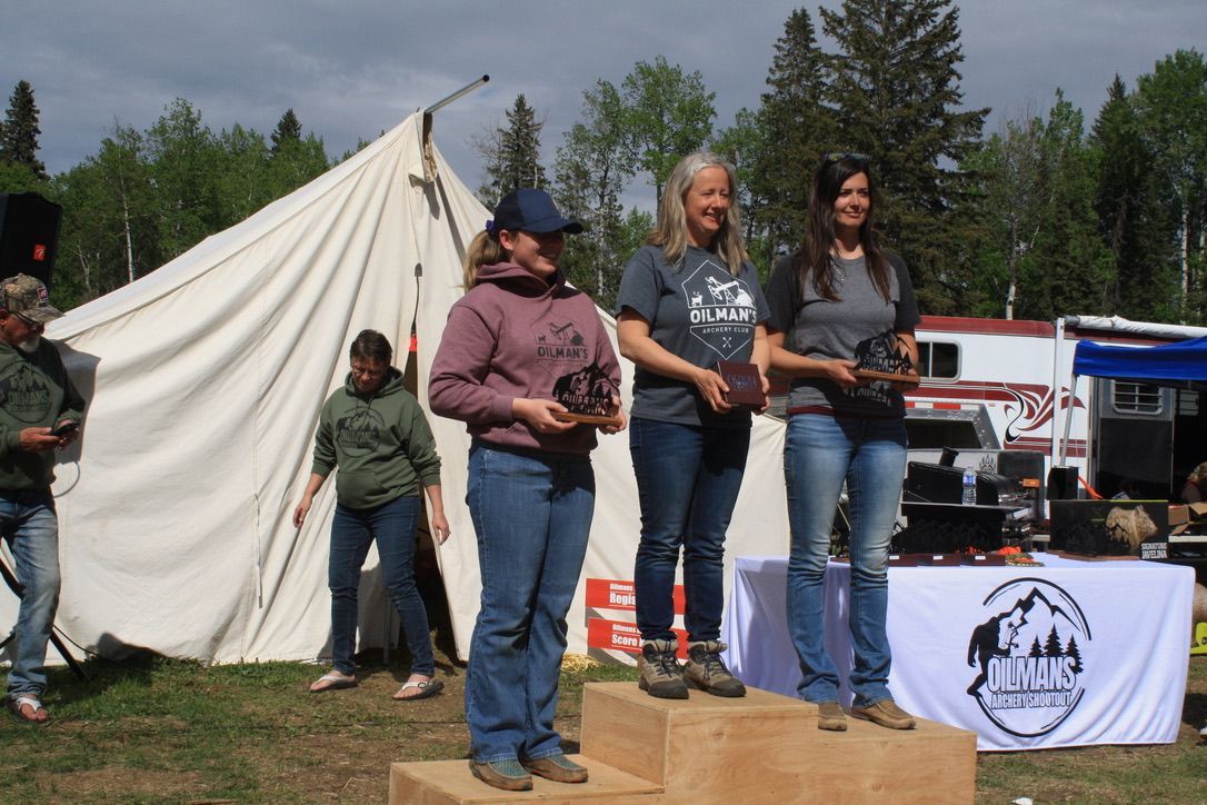 Three women are standing on a wooden podium in front of a tent.