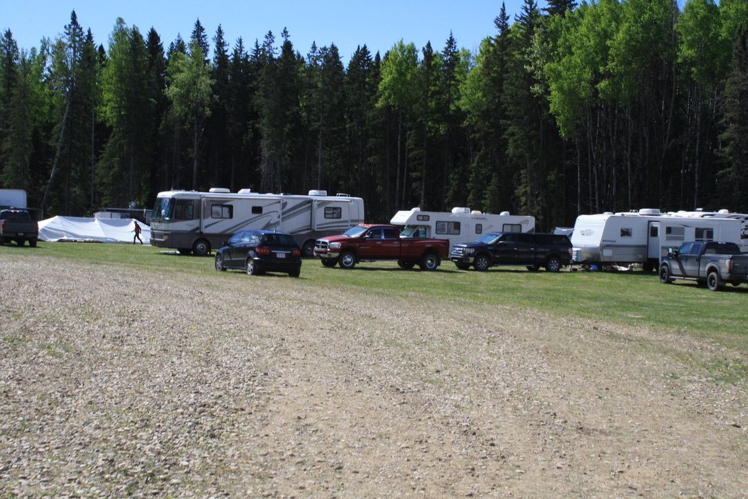 A row of rvs are parked in a field with trees in the background