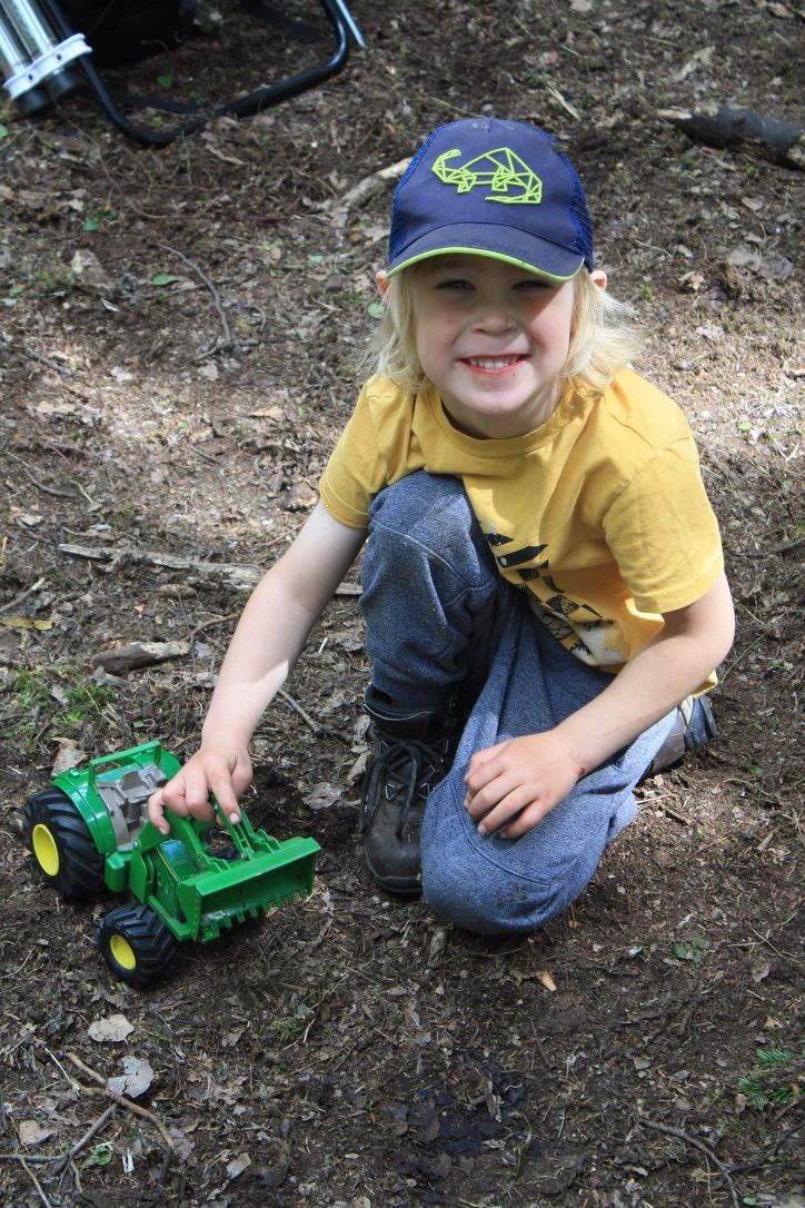 A young boy is kneeling down in the dirt playing with a toy tractor.