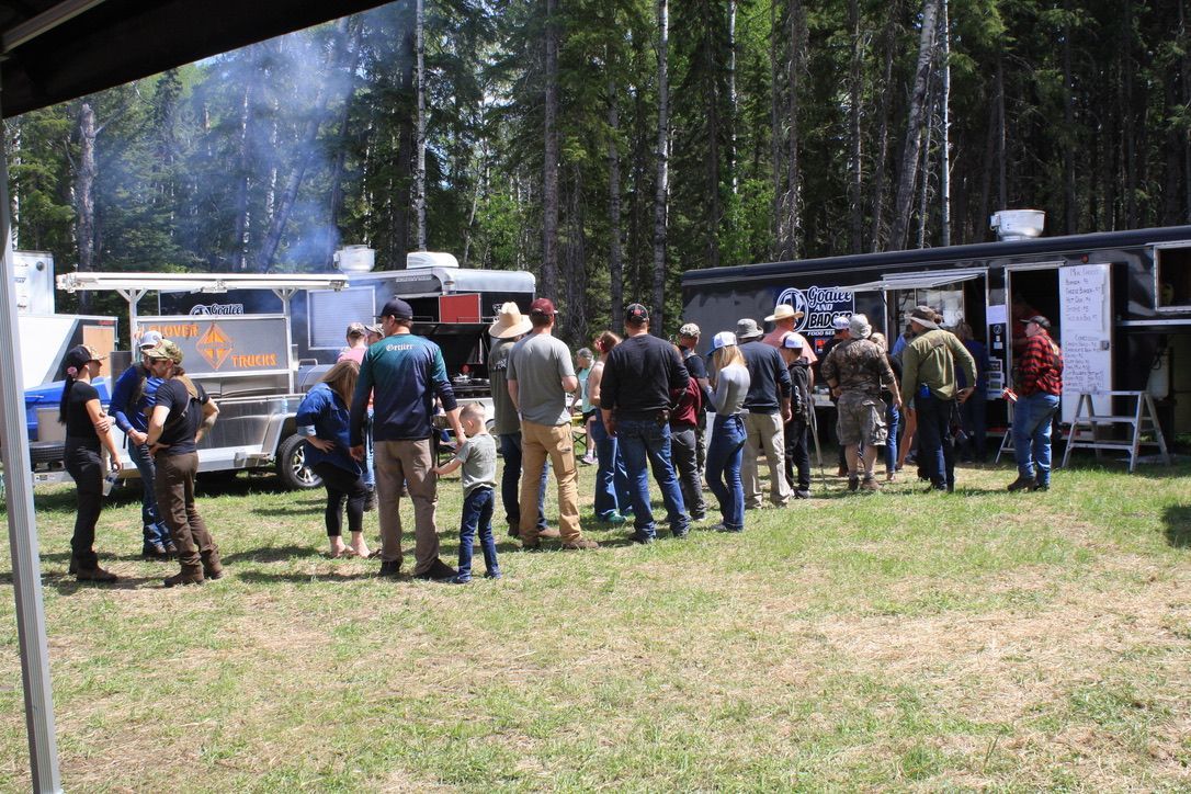 A group of people are standing in a field in front of food trucks.