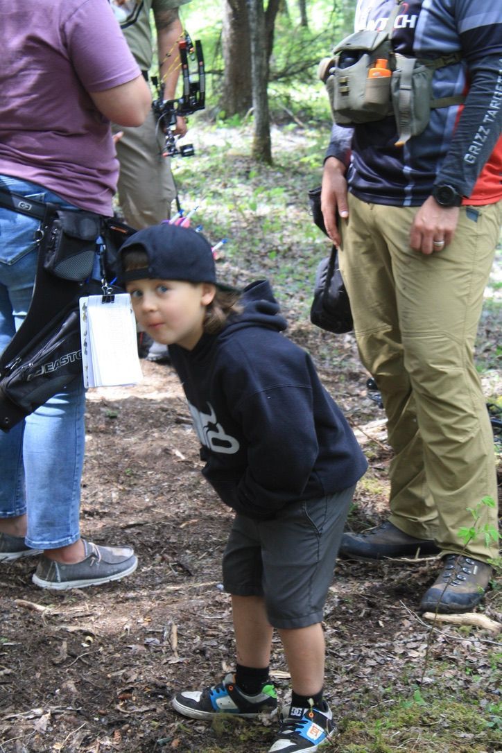A young boy wearing a baseball cap is standing in the woods.
