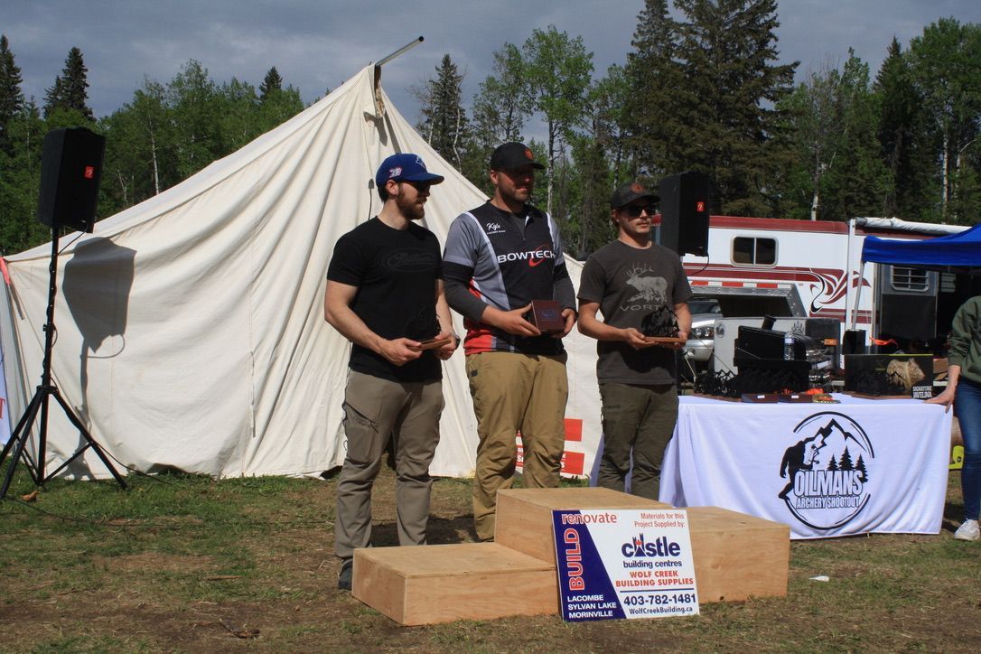 Three men are standing on a podium in front of a tent.