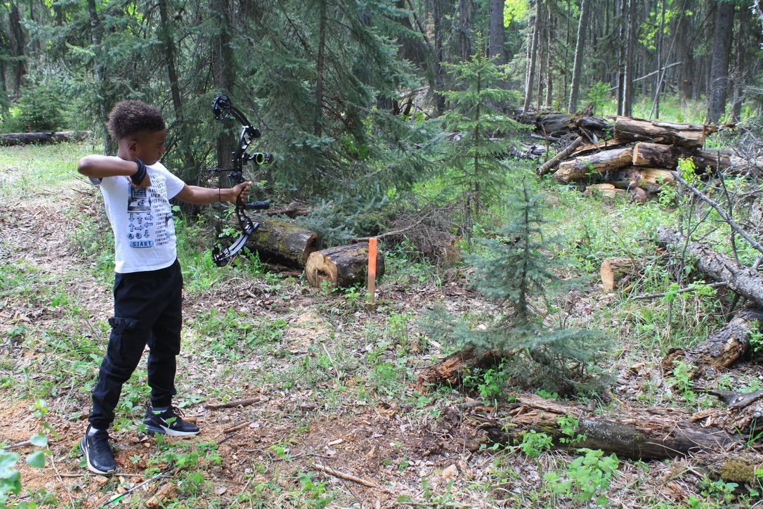 A young boy is practicing archery in the woods.