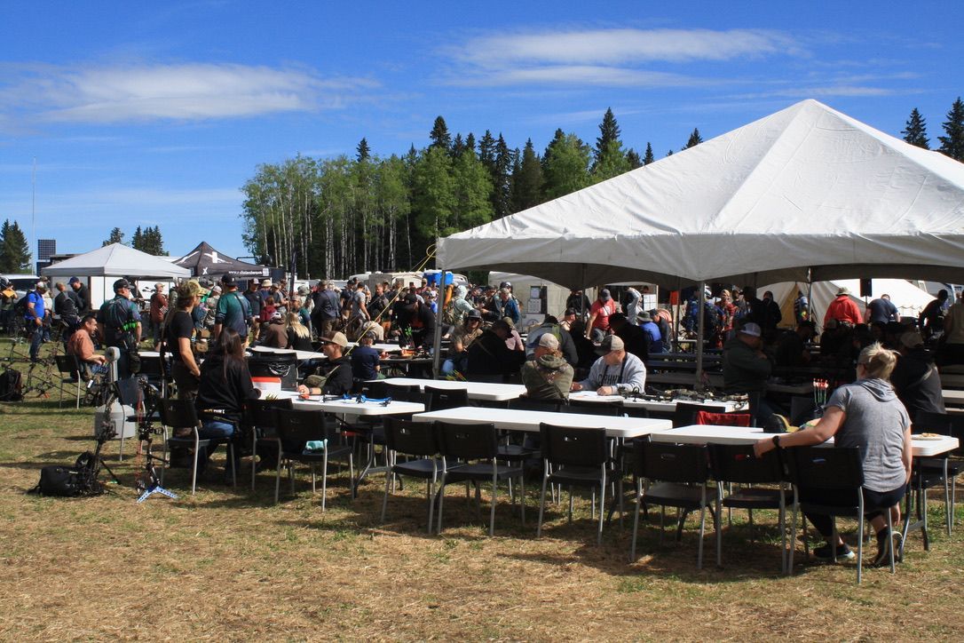 A group of people are sitting at tables under a tent in a field.