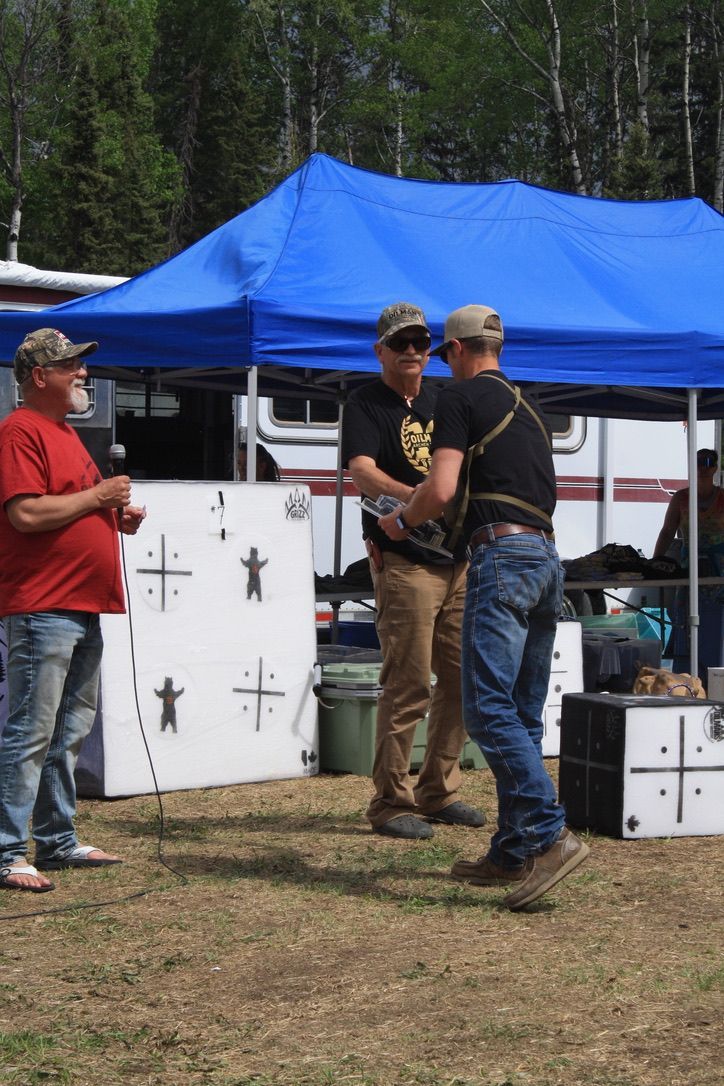 Three men are standing under a blue tent in a field.