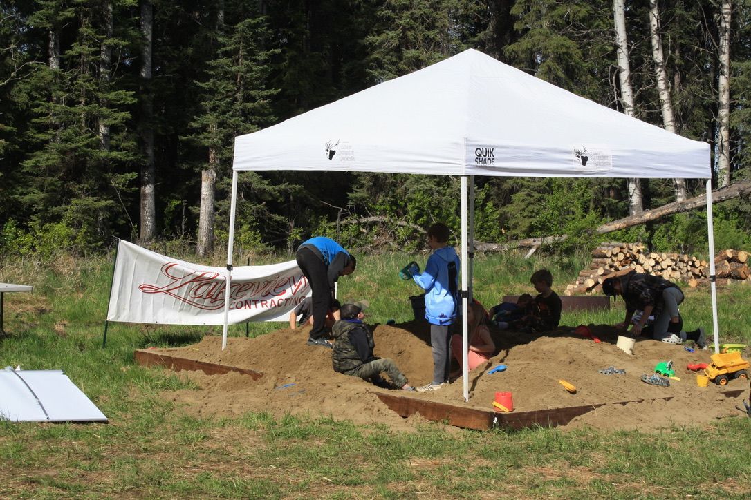 A group of people are playing in a sandbox under a white tent.