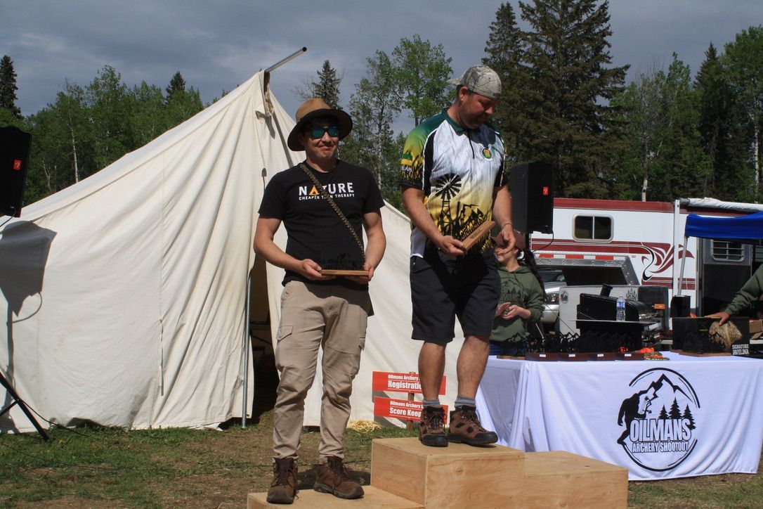 Two men are standing on a wooden podium in front of a tent.