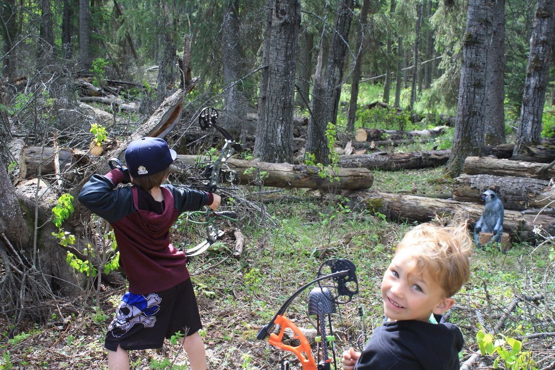 Two young boys are playing with bows and arrows in the woods.