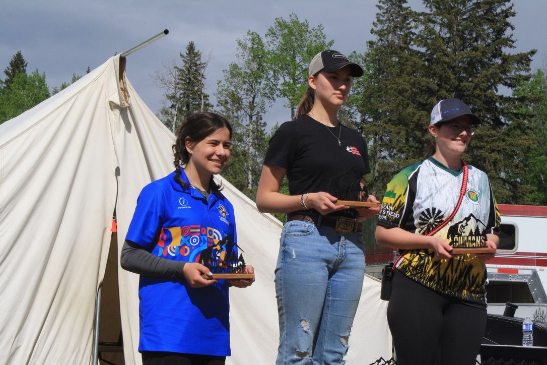 Three women are standing in front of a tent holding trophies.