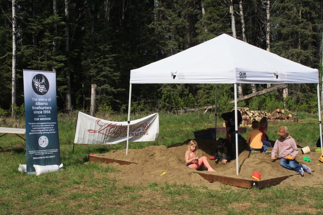 A group of people are playing in a sandbox under a white tent.