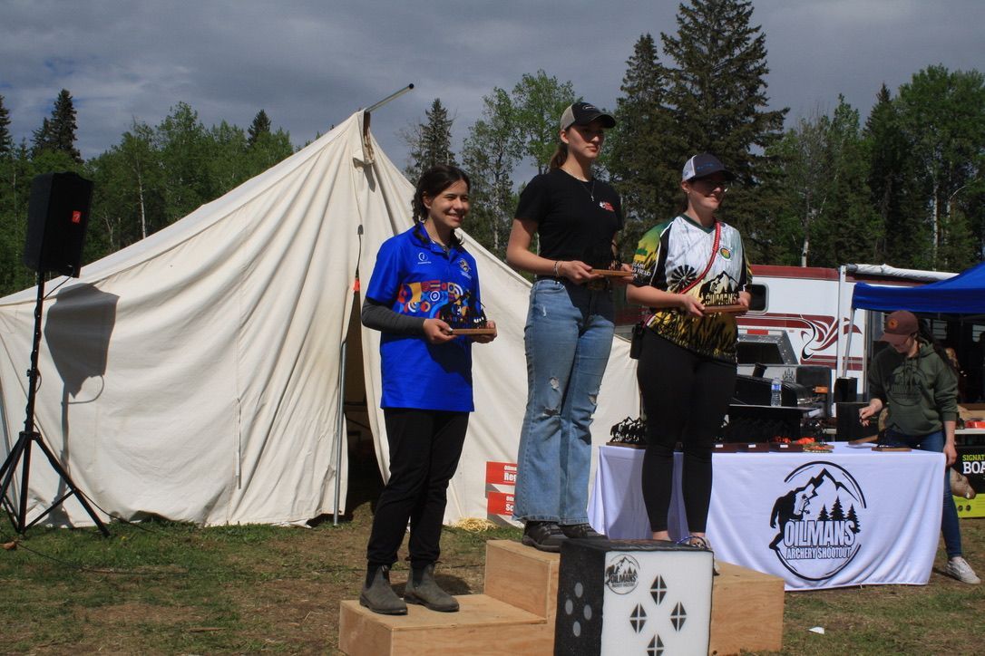 Three women are standing on a podium in front of a tent.