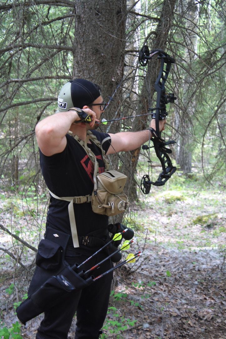 A man is holding a bow and arrows in the woods.