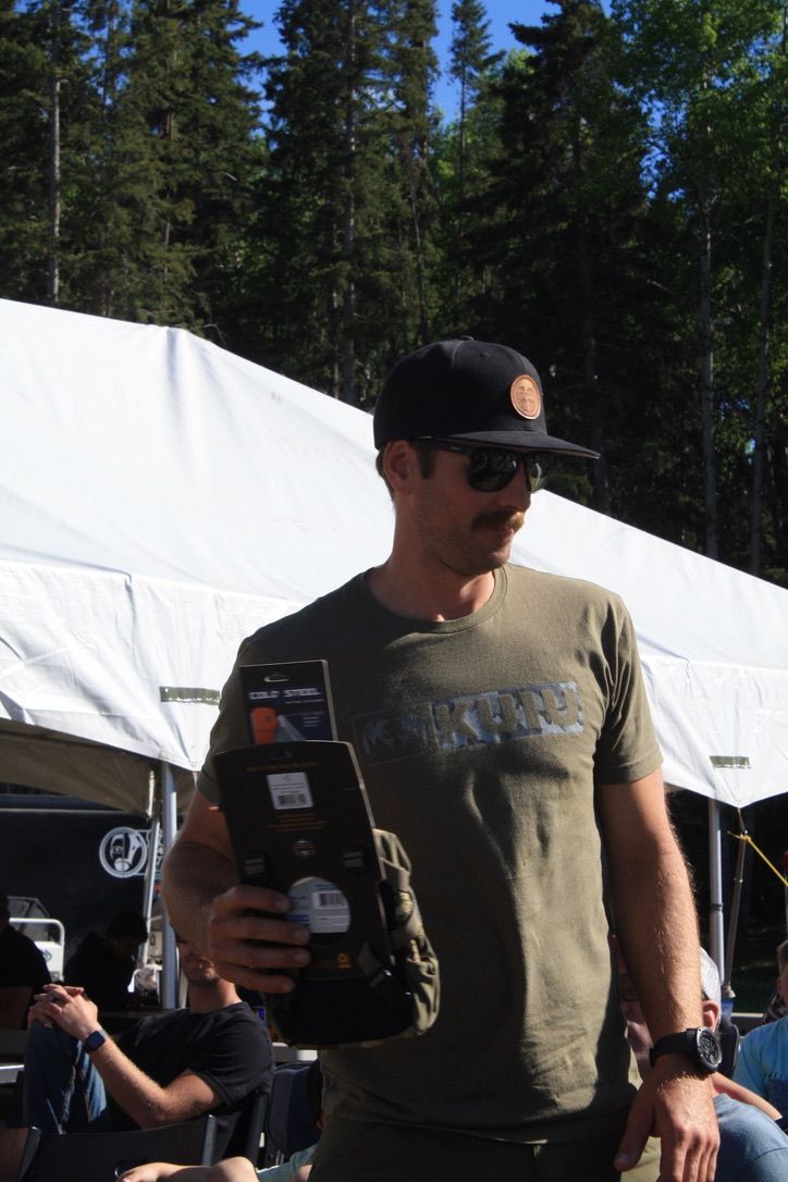 A man wearing a hat and sunglasses is holding a book in front of a tent.