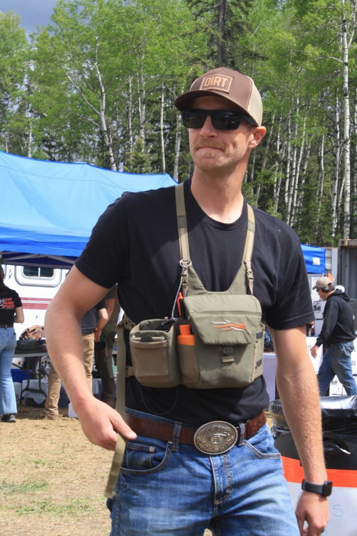 A man wearing a hat and sunglasses is standing in front of a blue tent.