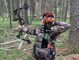 A man is holding a bow and arrows in the woods.