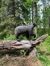 A statue of a black bear standing on top of a log in the woods.