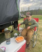 A young boy is sitting in a folding chair next to a cooler.