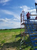A man is standing on top of a scaffolding in a field.