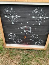 A chalkboard with arrows and a bear on it is sitting in the grass.