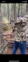 A man in a camouflage shirt is standing in the woods with a hammer.