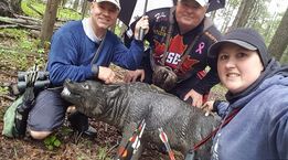 A group of people are posing for a picture with a boar in the woods.