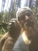 A man with a beard is kissing a bigfoot in the woods.