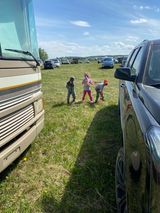 A group of children are playing in a field next to a truck and a rv.
