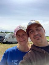 A man and a woman are posing for a selfie in front of a camper trailer.