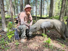 A man is sitting next to a statue of a bear in the woods.