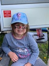A little girl with her face painted is sitting on a bench.