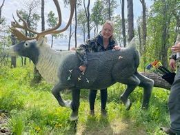 A woman is standing next to a deer statue in the woods.