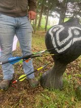 A man is standing next to a target with arrows in it.