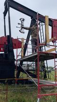 A man is standing on a scaffolding next to an oil pump.