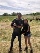 A man and a girl are standing in a field holding a puppy.
