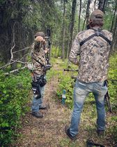 Two men are standing in the woods with bows and arrows.